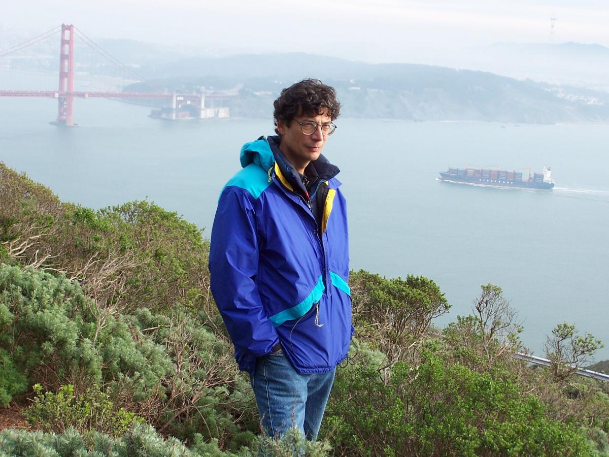 Man in blue jacket standing on hill overlooking Golden Gate Bridge