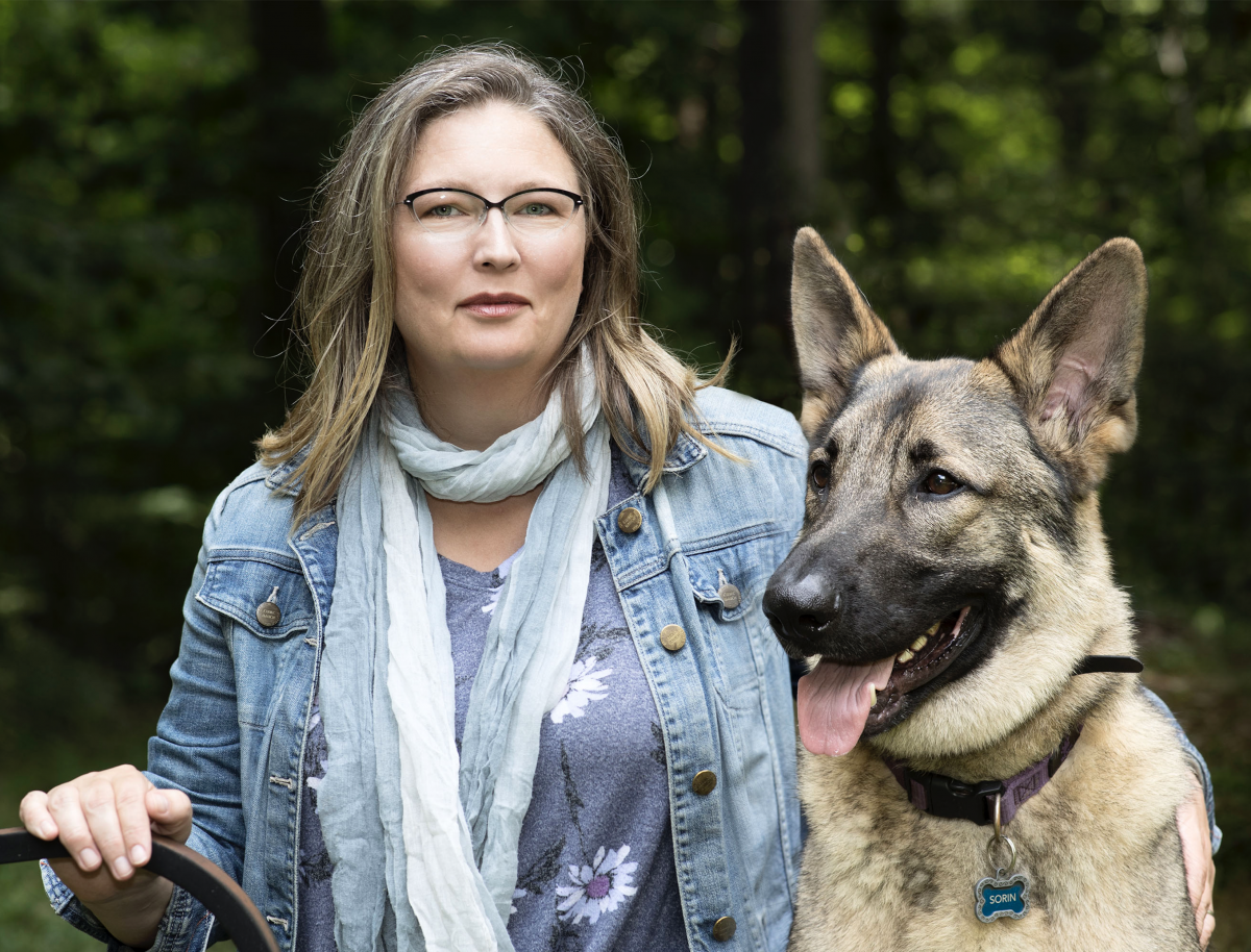 Closeup of a woman in a denim blue jacket and blue scarf, sitting beside a large dog