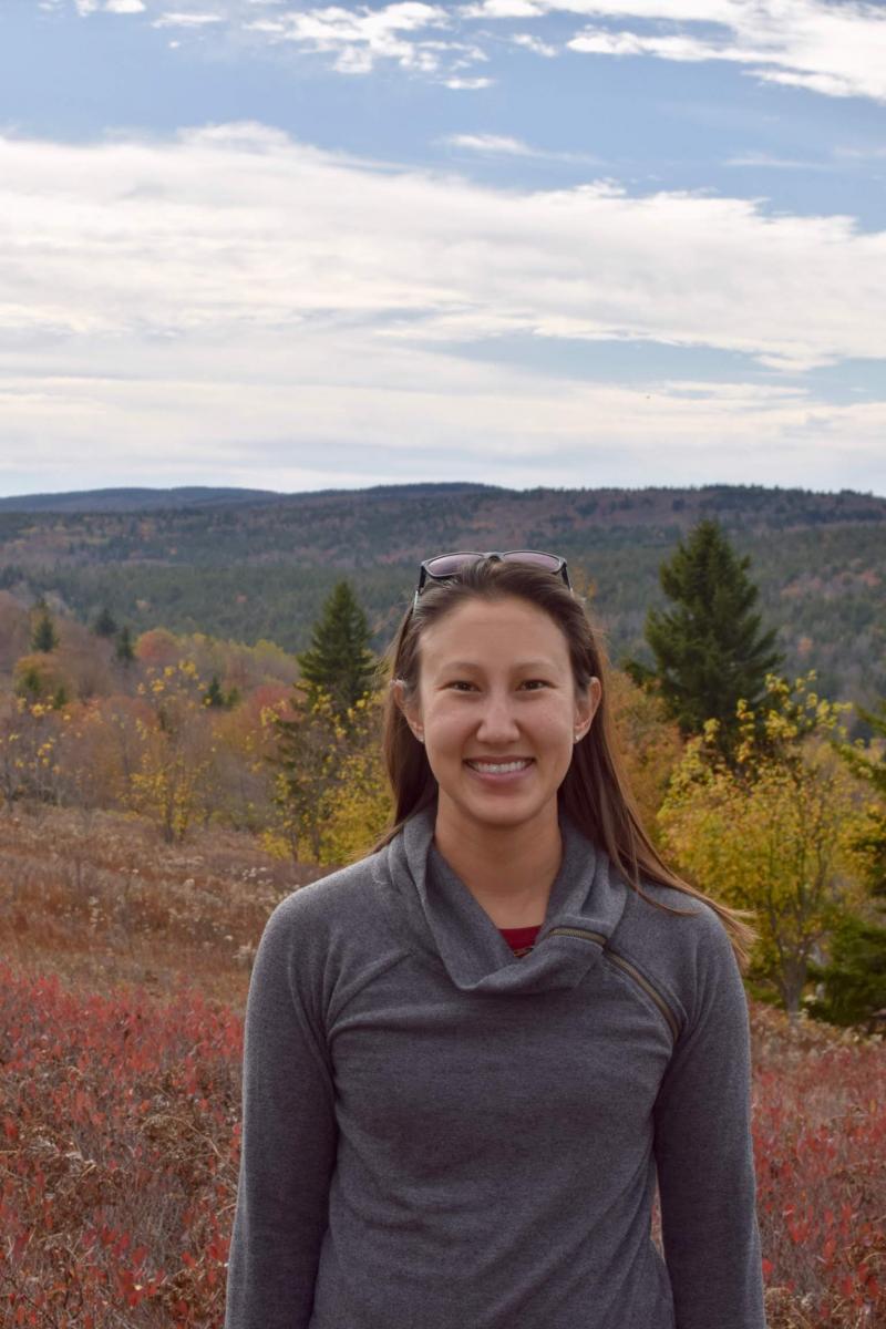 Head and shoulders picture of woman standing on mountain with red and yellow fall colors in the background