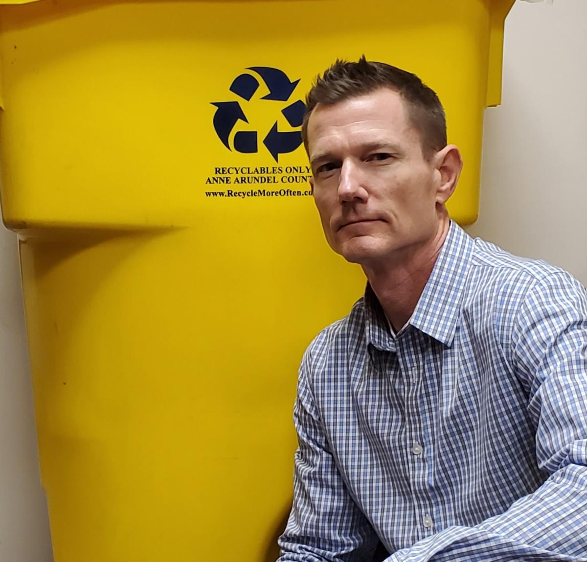 Man kneeling beside yellow recycling cart