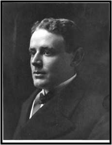 Black and white photo of a young man in a black business suit with a neutral expression on his face. He is in profile, with his face turned slightly toward the camera so his full face is visible.