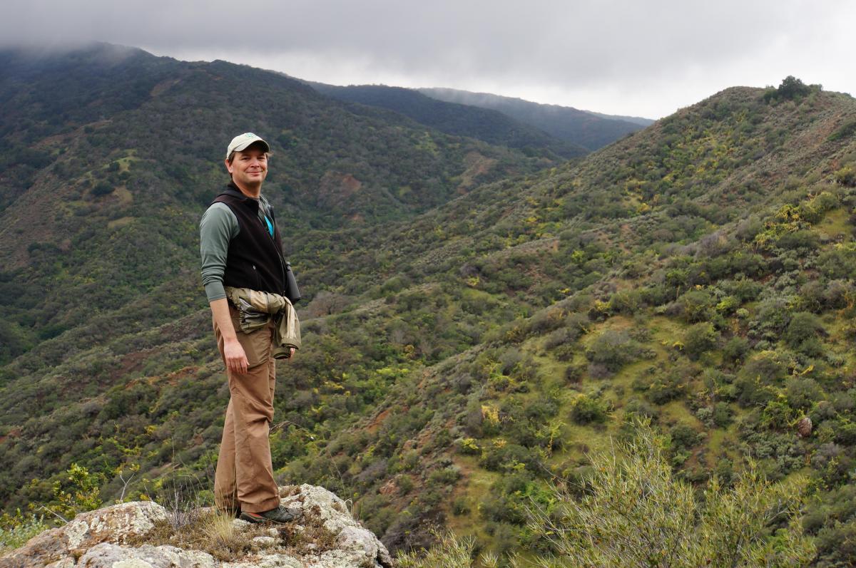 Man standing on rocky ledge in a misty mountain range