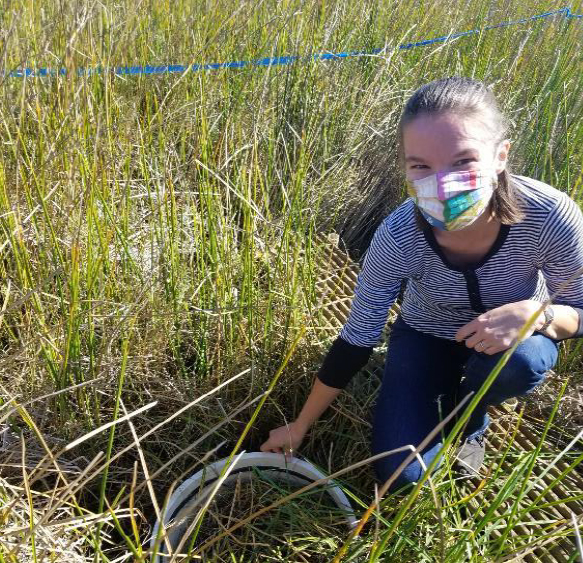 Young woman kneeling in grassy wetland wearing a multicolored face mask