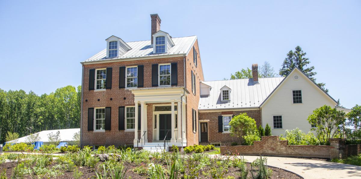 Front of a three-section house, with two brick sections and one section with white siding. The largest section on the left is three stories of brick, with a white-columned front porch.