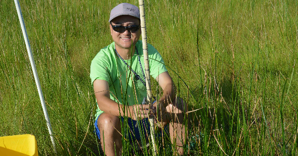 Young man in green T-shirt sitting in a marsh with a measuring stick