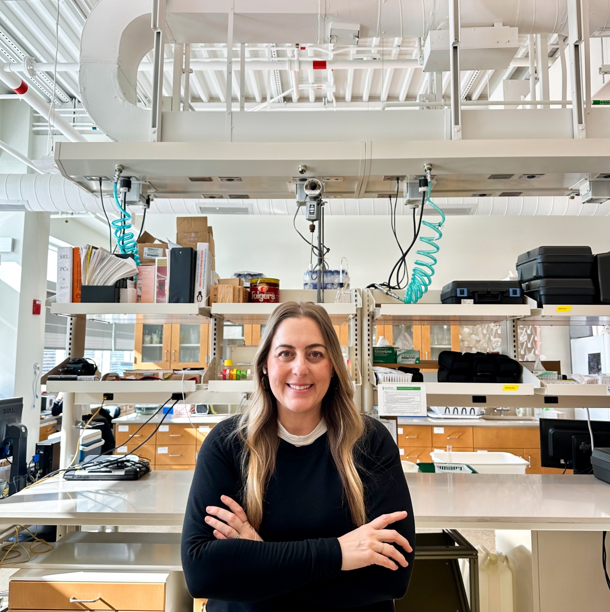 Tara Sill wearing a black long sleeve shirt posing in front of a science laboratory with shelves