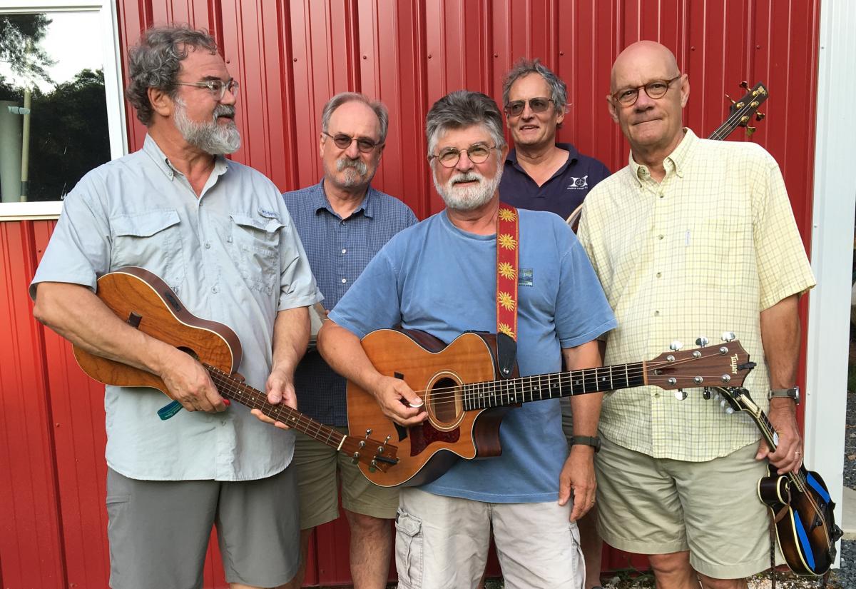 Five men in front of a red house, three with guitars