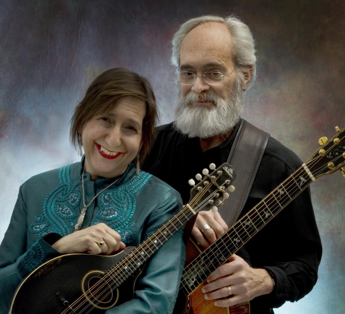 A woman and man standing together holding guitars