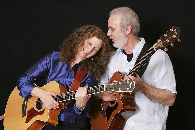 A woman and a man playing guitars together