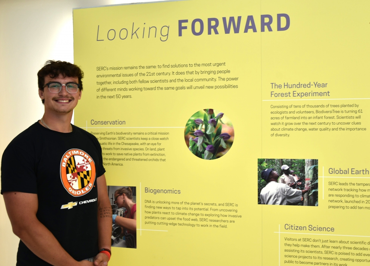 Intern Matt Lepper posing in front of a science poster titled Looking Forward