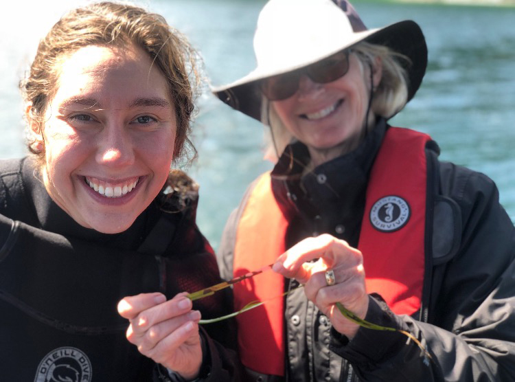 Two women hold up infected eelgrass blade