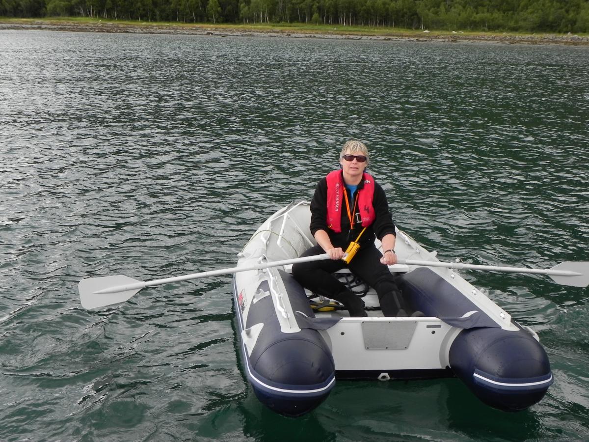 Woman in a red life preserver rows a gray boat with two paddles through the water