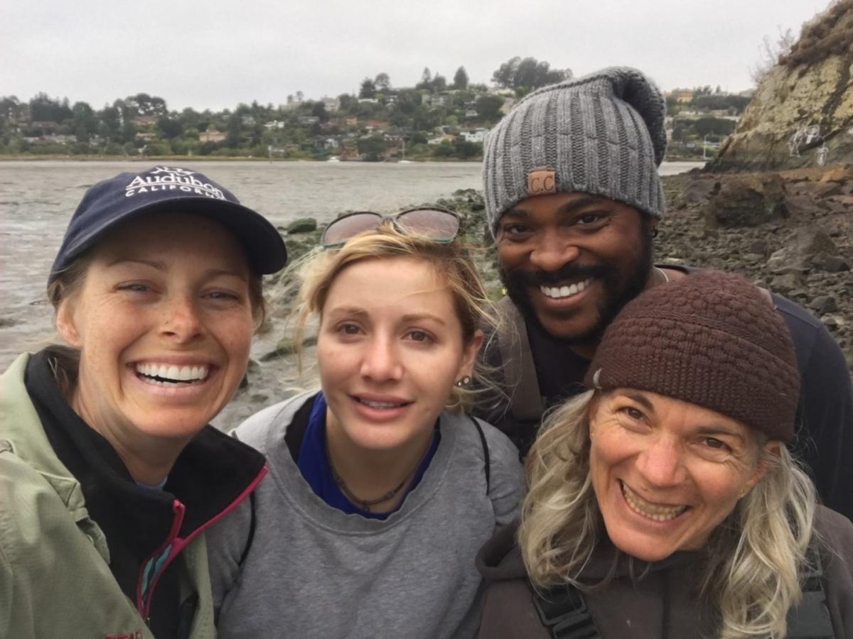 Four scientists pose for a selfie in front of a rocky shoreline