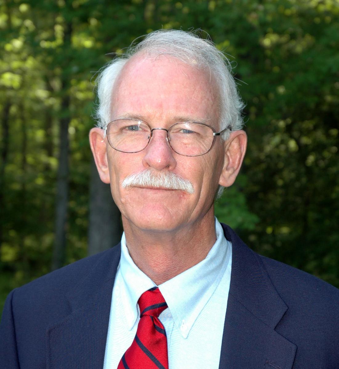 Tuck Hines in a navy suit, with white hair, mustache and glasses