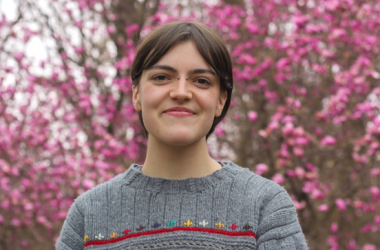 Anna smiles at the camera while posing with a pink flower background.