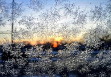 Sharp close-up of icy snowflakes, with a blurry blue, gold and orange sunrise in the background