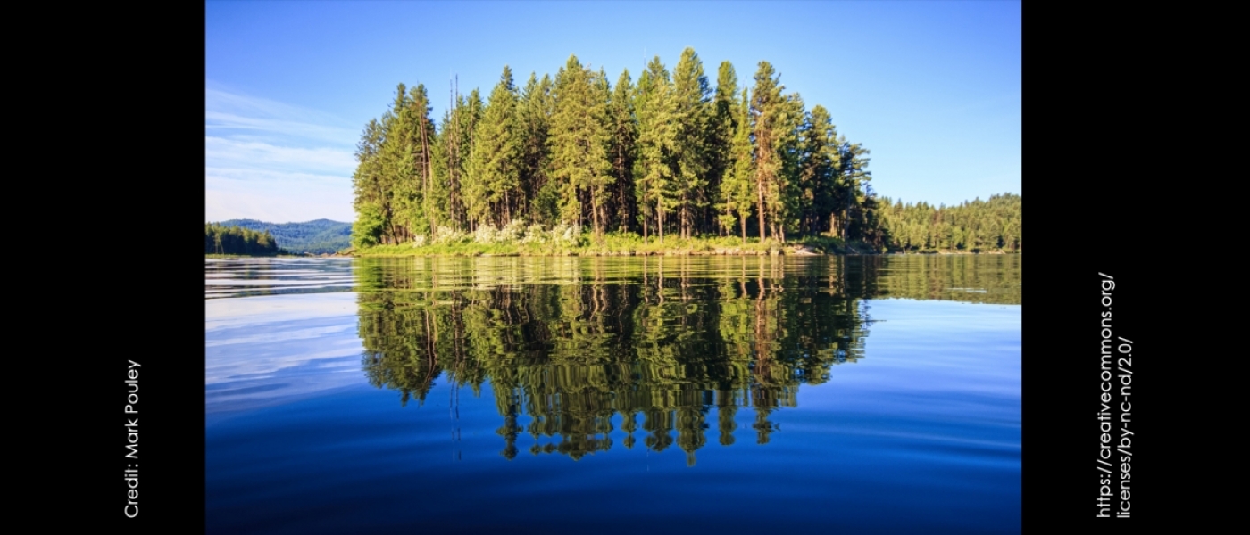 Trees on the shore of North Twin Lake reflect off the still blue waters. Credit: Mark Pouley