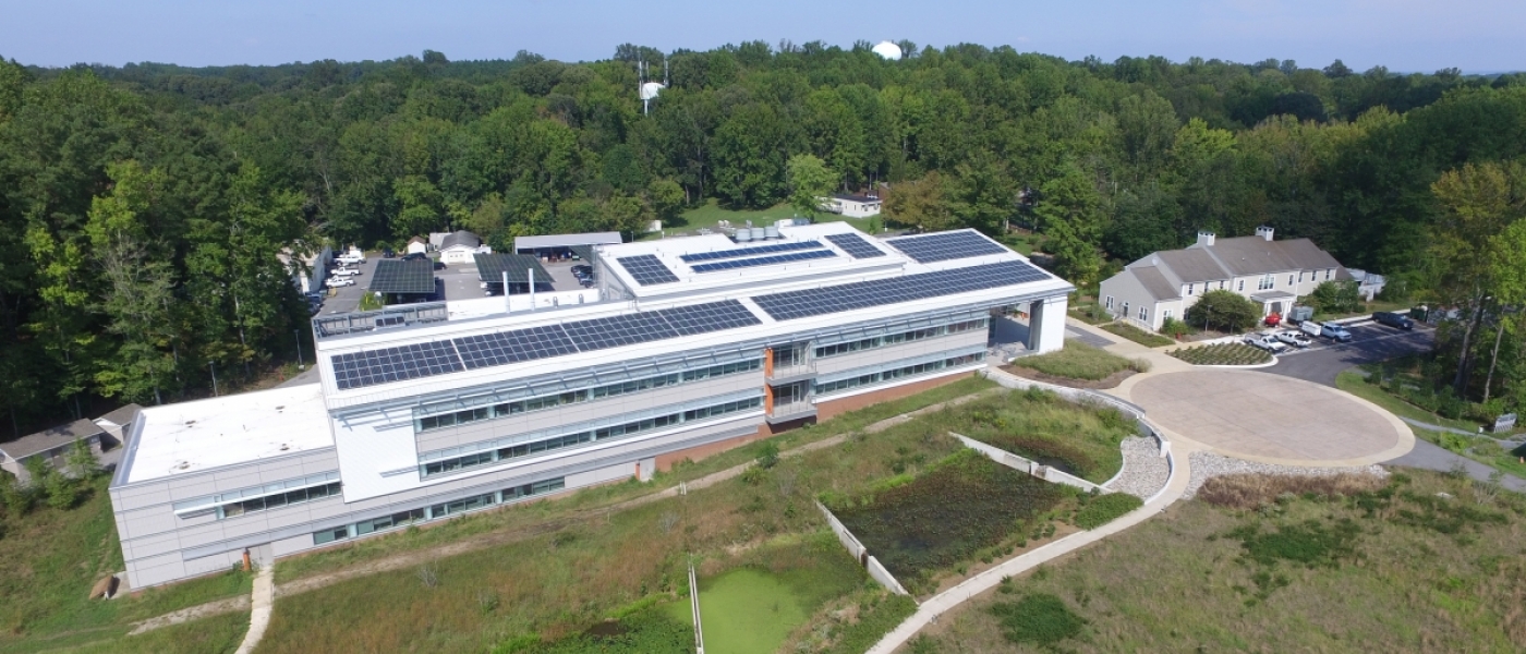 Aerial view of a research lab with rooftop solar panels, surrounded by a green forest and wetland