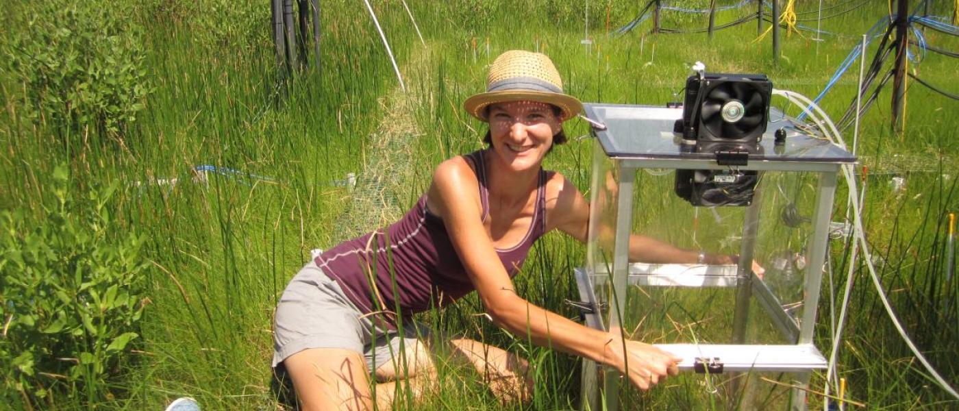 Young woman sitting in a marsh, holding a transparent experimental chamber