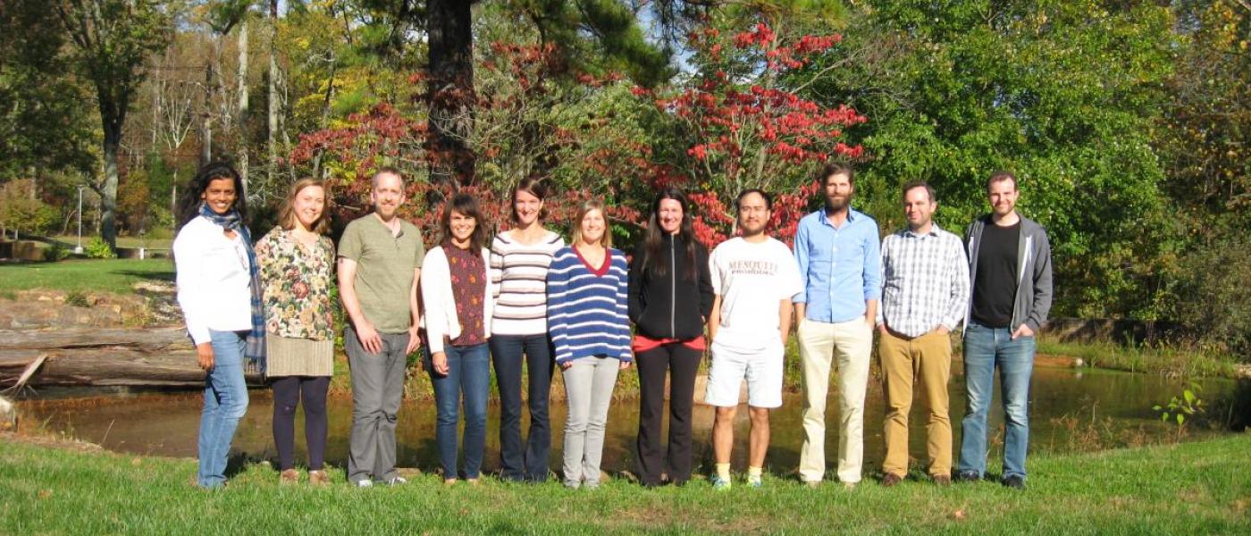 11 research postdoctoral fellows pose for a group picture on the grass, in front of a pond