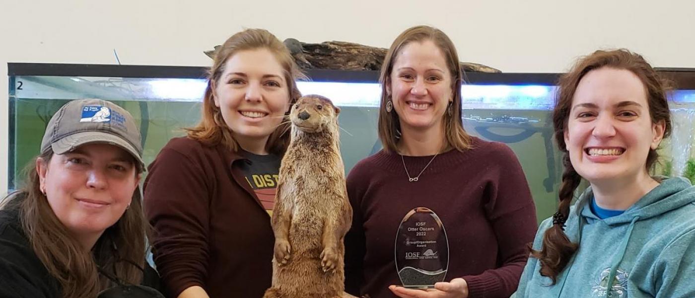 4 Chesapeake Bay Otter Alliance team members posing with a life-like otter sculpture and their otter award.