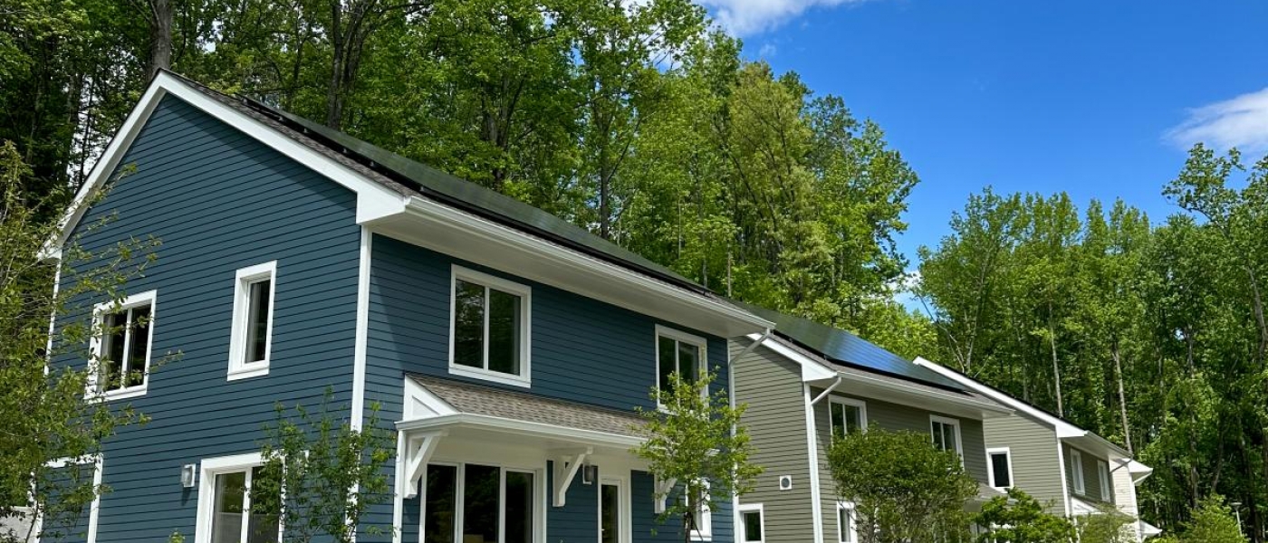 Three two-story cottages with rooftop solar panels between a forest and a road