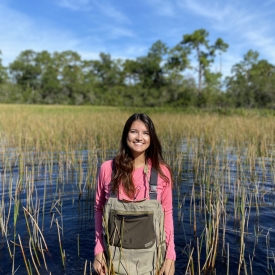 Chelsea Nitsch standing in a wetland, wearing waders and a pink shirt