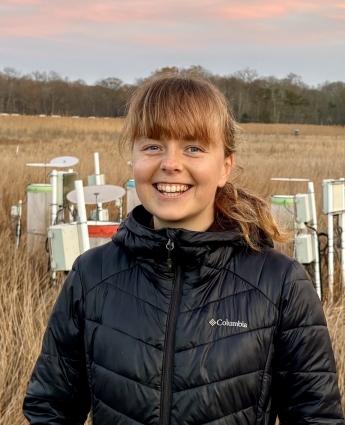 Abigail Lewis standing in a marsh with experimental chambers