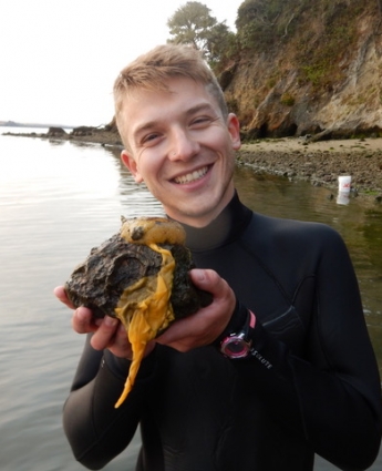Benjamin Rubinoff stands in shallow water holding a rock with a sea lemon nudibranch on it.