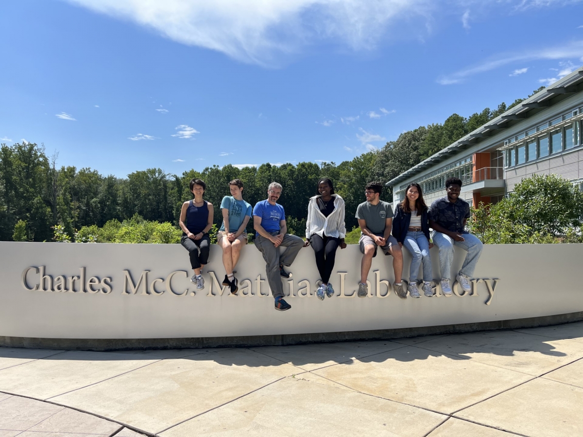 A group of six people sitting on the Charles McC. Mathis Laboratory sign on a sunny blue sky day.